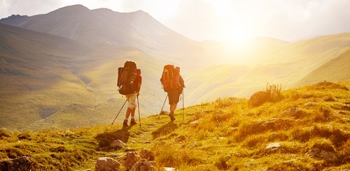 zwei Wanderer laufen in einer wilden Landschaft in Abendsonne auf einem Weg