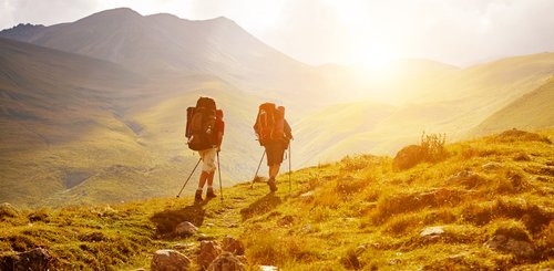 zwei Wanderer laufen in einer wilden Landschaft in Abendsonne auf einem Weg