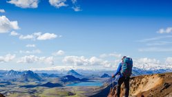 Eine Person in Outdoorkleidung schaut über die bergige Landschaft Islands