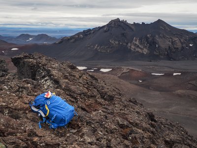 Eine Vulkanlandschaft aus alter Lava mit einem blauen Rucksack als Kontrast.