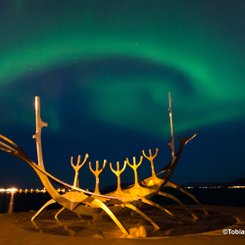 Über der Statue Sun Voyager in Reykjavik kringelt sich ein grünes Polarlicht. Das Zeichen des Großen Wagen ist auch zu erkennen.