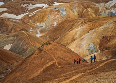 Eine Gruppe aus sechs Personen läuft einen Pfad im Kerlingarfjöll-Gebiet von rechts nach links. Der Boden ist zimtfarben. 