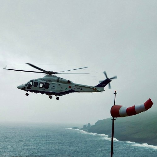 Hubschrauber fliegt von rechts nach links, eine Windhose hzeigt sehr stürmisches Wetter an.