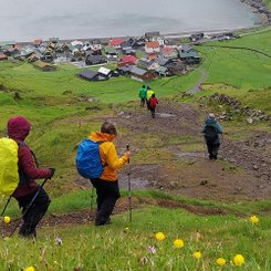 Die Wandergruppe steigt von einer Anhöhe in den Dorf Tjörnuvik auf den Färöern hinab