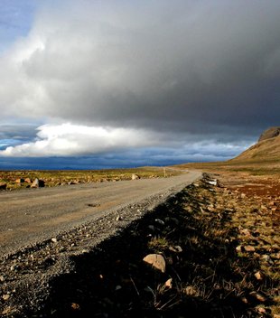 Individueller Island Urlaub - Tiefstehende Sonne und Wolken über geschotterter isländischer Landstraße
