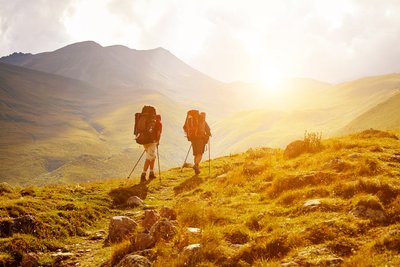zwei Wanderer laufen in einer wilden Landschaft in Abendsonne auf einem Weg