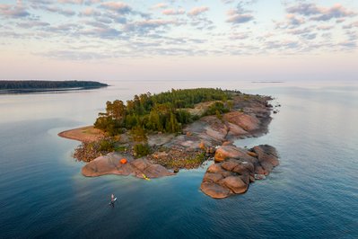 Eine Insel aus der Vogelperspektive in einem Schärengebiet in Finnland. Man sieht einen Kajakfahrer. 
