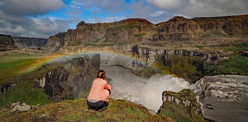 Wanderin am Wasserfall Hafragilsfoss mit Regenbogen