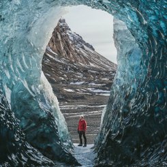 Eishöhle mit Mensch in roter Outdoorjacke am Vatnajökull in Island