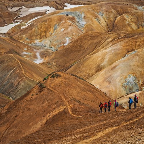 Eine Gruppe aus sechs Personen läuft einen Pfad im Kerlingarfjöll-Gebiet von rechts nach links. Der Boden ist zimtfarben. 