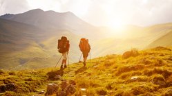 zwei Wanderer laufen in einer wilden Landschaft in Abendsonne auf einem Weg