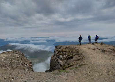 Drei Personen stehen am Rand der Klippe am höchsten Berg der Färöer-Inseln
