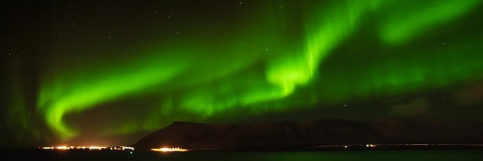 Nur auf Nordland Reisen im Winter - Grüne Nordlichter über Fjord mit beleuchtetem Ort