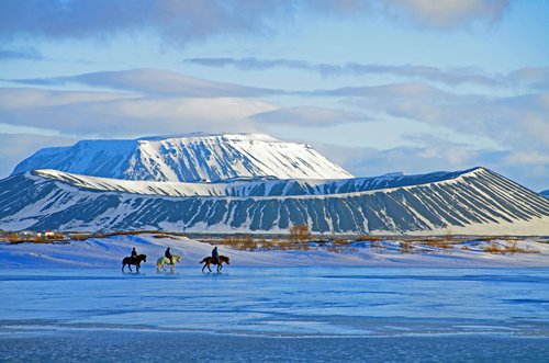 Drei Reiter auf dem gefrorenen See Myvatn im Norden Islands. ImHintergrund ist der Berg Hverfell zu sehen. 