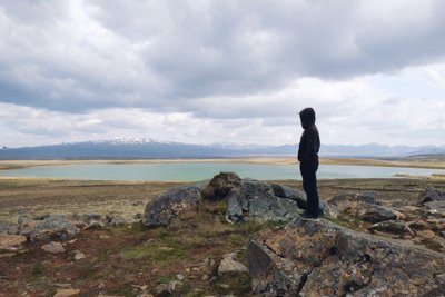 Person steht auf einem felsigen Untergrund mit Blick auf eine weite Hochlandlandschaft in Island