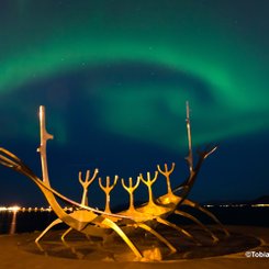 Über der Statue Sun Voyager in Reykjavik kringelt sich ein grünes Polarlicht. Das Zeichen des Großen Wagen ist auch zu erkennen.