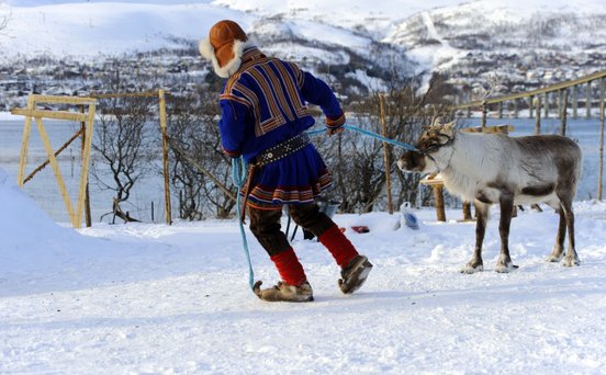 Ein Sami in traditioneller Kleidung führt ein Rentier durch den Schnee