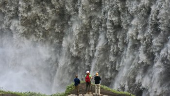 Ein nachhaltiges Erlebnis auf Island Reisen - Besucher vor der schäumenden Wasserwand des gewaltigen Wassersfalls Dettifoss