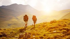 zwei Wanderer laufen in einer wilden Landschaft in Abendsonne auf einem Weg
