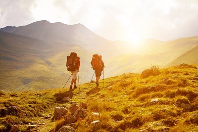 zwei Wanderer laufen in einer wilden Landschaft in Abendsonne auf einem Weg