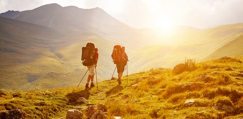 zwei Wanderer laufen in einer wilden Landschaft in Abendsonne auf einem Weg