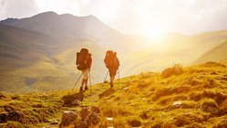 zwei Wanderer laufen in einer wilden Landschaft in Abendsonne auf einem Weg