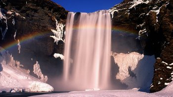 Island auf Winterreisen - Wasserfall im Winterkleid mit Regenbogen