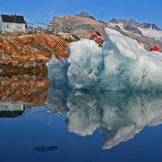 Ein typisches Bild im Grönland Urlaub - Eisberg vor Felsküste mit bunten Häusern