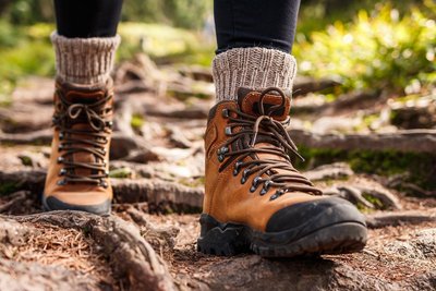 Ein Mensch in Wanderschuhen und Wollsocke läuft über einen verwurzelten Boden.