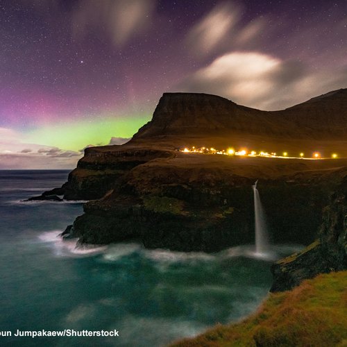 Über dem beliebten Motiv am Ort Gásadalur mit Wasserfall sieht man leichte Polarlichter