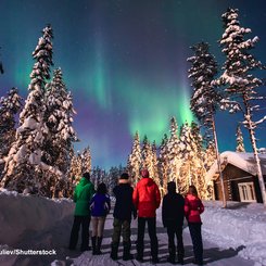 Eine Gruppe Menschen steht auf einem verschneiten Weg und bestaunt Polarlichter am Himmel in Lappland/Norwegen