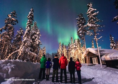 Eine Gruppe Menschen steht auf einem verschneiten Weg und bestaunt Polarlichter am Himmel in Lappland/Norwegen