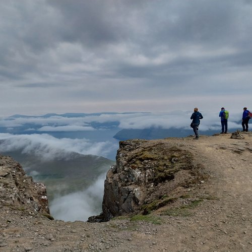 Drei Personen stehen am Rand der Klippe am höchsten Berg der Färöer-Inseln