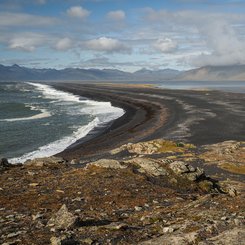 Ein langgezogener schwarzer Strand vor einem Bergpanorama