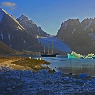 Urlaub in Spitzbergen - Segelschiff im Fjord mit Eisbergen vor Gletscher und steilen Bergen