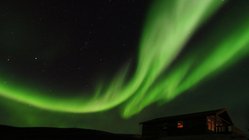 Am Nachthimmel über einem Ferienhaus tanzt ein grüner Nordlichtschweif
