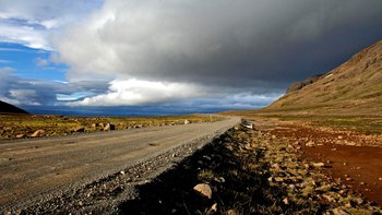 Individueller Island Urlaub - Tiefstehende Sonne und Wolken über geschotterter isländischer Landstraße